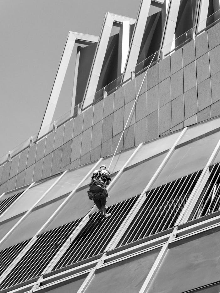 A black and white image of a window cleaner scaling a modern building.